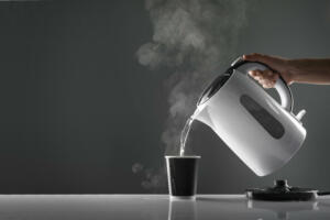 Electric white kettle pouring water in cup on table on grey background