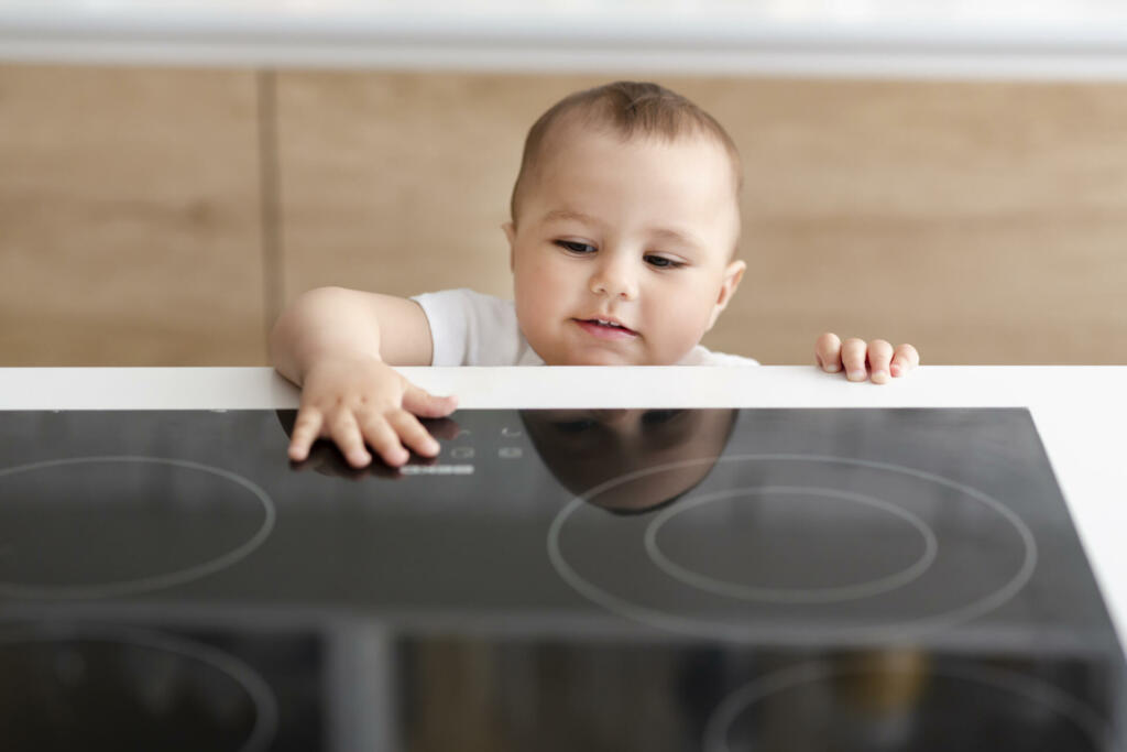 Hazard at kitchen. Curious toddler reaching hand to hot electric cooktop, free space