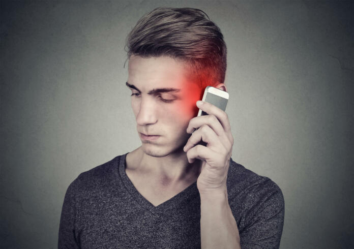 Man on the cellphone with headache. Upset unhappy guy talking on a phone isolated on gray wall background. Negative human emotion face expression feeling reaction.