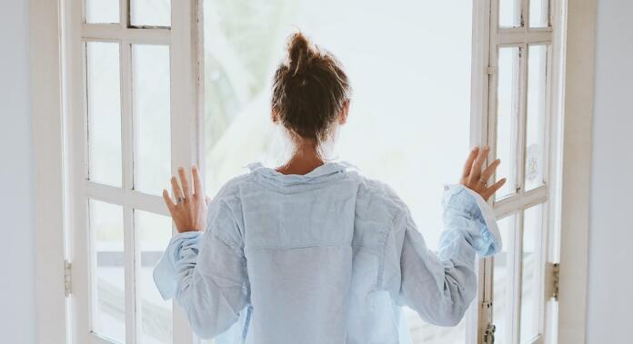 Ženska v spalni srajci odpira okno