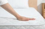 Woman touching soft white mattress on bed indoors, closeup