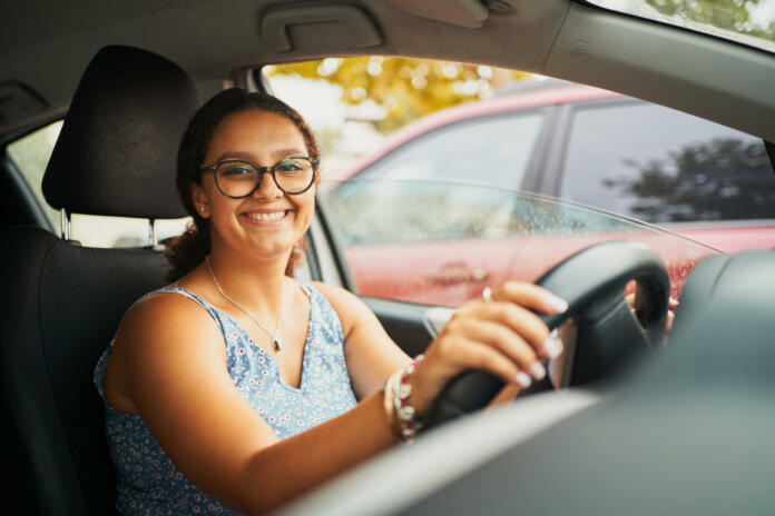 Young brunette spanish woman sitting on car smiling at camera