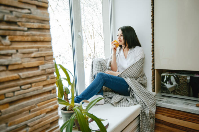 young and pretty brunette sitting by the window in the kitchen with lemon