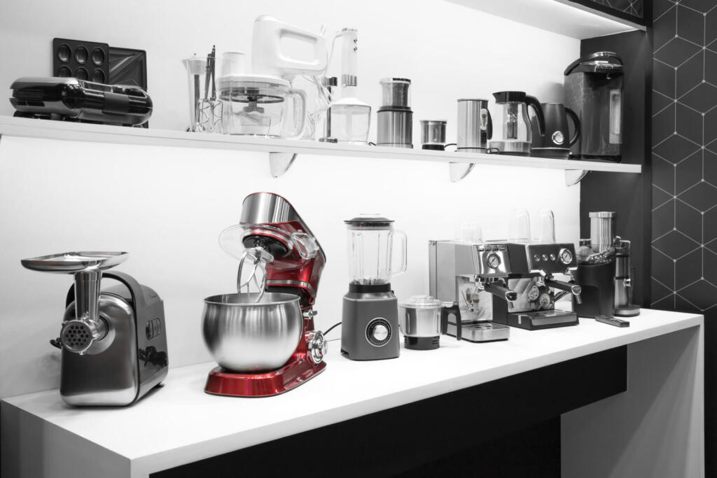 Household appliances for the kitchen. Sale of electrical equipment for cooking at home. Coffee makers, mixers, meat grinders, blenders, coffee machines, toasters and kettles on a shelf in the interior.