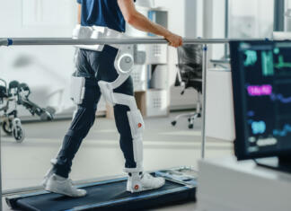 Robot, ki bo ljudem ponovno pomagal shoditi… Modern Hospital Physical Therapy: Patient with Injury Walks on Treadmill Wearing Advanced Robotic Exoskeleton Legs. Physiotherapy Rehabilitation Technology to Make Disabled Person Walk. Focus on Legs