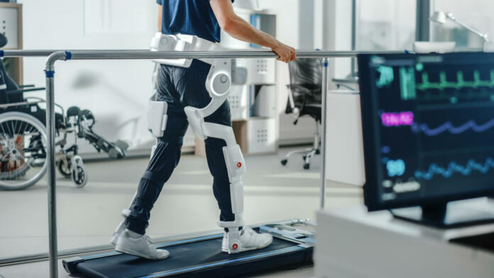 Modern Hospital Physical Therapy: Patient with Injury Walks on Treadmill Wearing Advanced Robotic Exoskeleton Legs. Physiotherapy Rehabilitation Technology to Make Disabled Person Walk. Focus on Legs