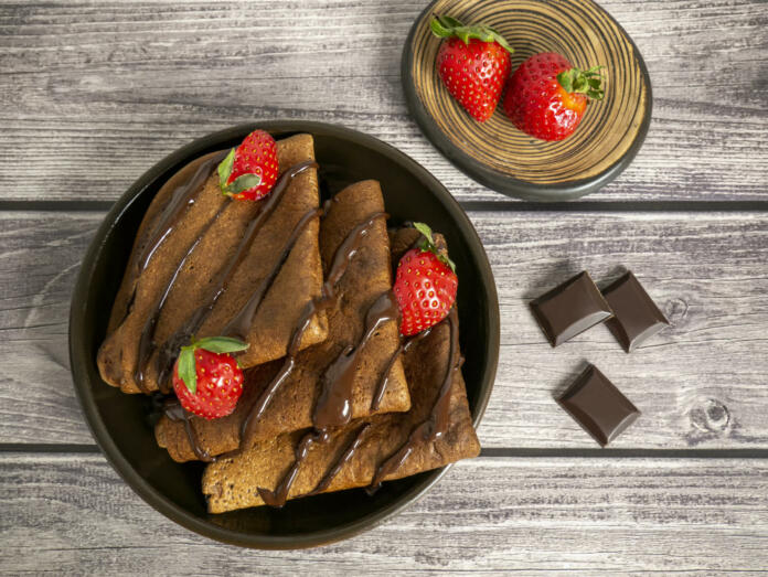 Pancakes made of chocolate dough with strawberries, poured with chocolate. Maslenitsa, a delicious sweet dessert.