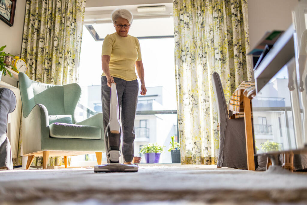 Senior woman using vacuum cleaner to clean the house