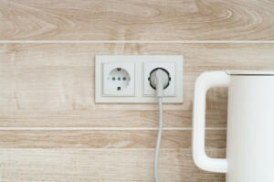 White electric kettle plugged into a power outlet on a wall into a kitchen