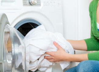 Bela oblačila so med pranjem posivela? Samo 3 kapljice tega v pralnem stroju bodo enkrat za vselej rešile težavo Young woman or housekeeper has a laundry day at home, she takes the laundry or whites out of your washing machine or the dryer