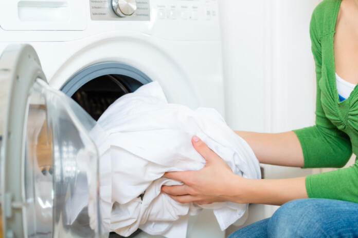 Young woman or housekeeper has a laundry day at home, she takes the laundry or whites out of your washing machine or the dryer