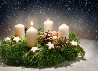Kaj je ‘advent’ in zakaj smo v nedeljo prižgali prvo svečko na venčku? Advent wreath from evergreen branches with white candles, the first is burning for the time before Christmas, dark snowy background with copy space, selected focus