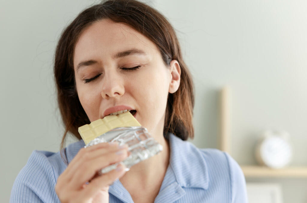 Cheerful young woman eating white chocolate bar at home