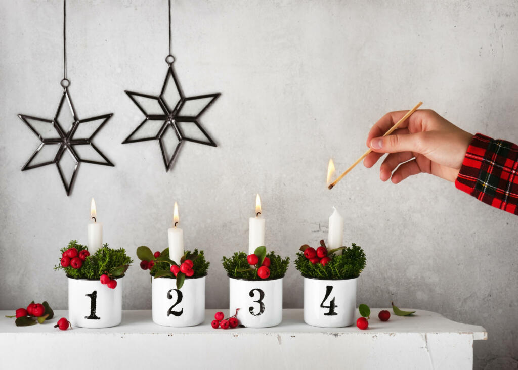 Girl hand lighting the fourth candle on a handmade advent wreath decorated with red checkerberries.Christmas home decoration concept. Copy space.
