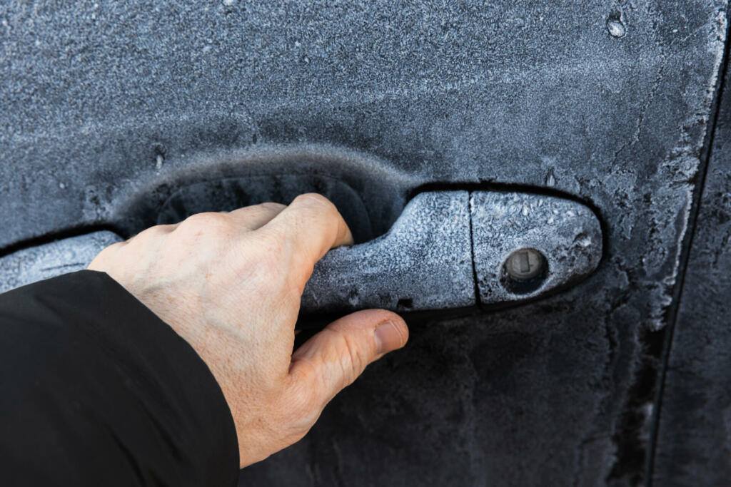 Hand trying to open locked door of a black car covered with frost in cold winter season