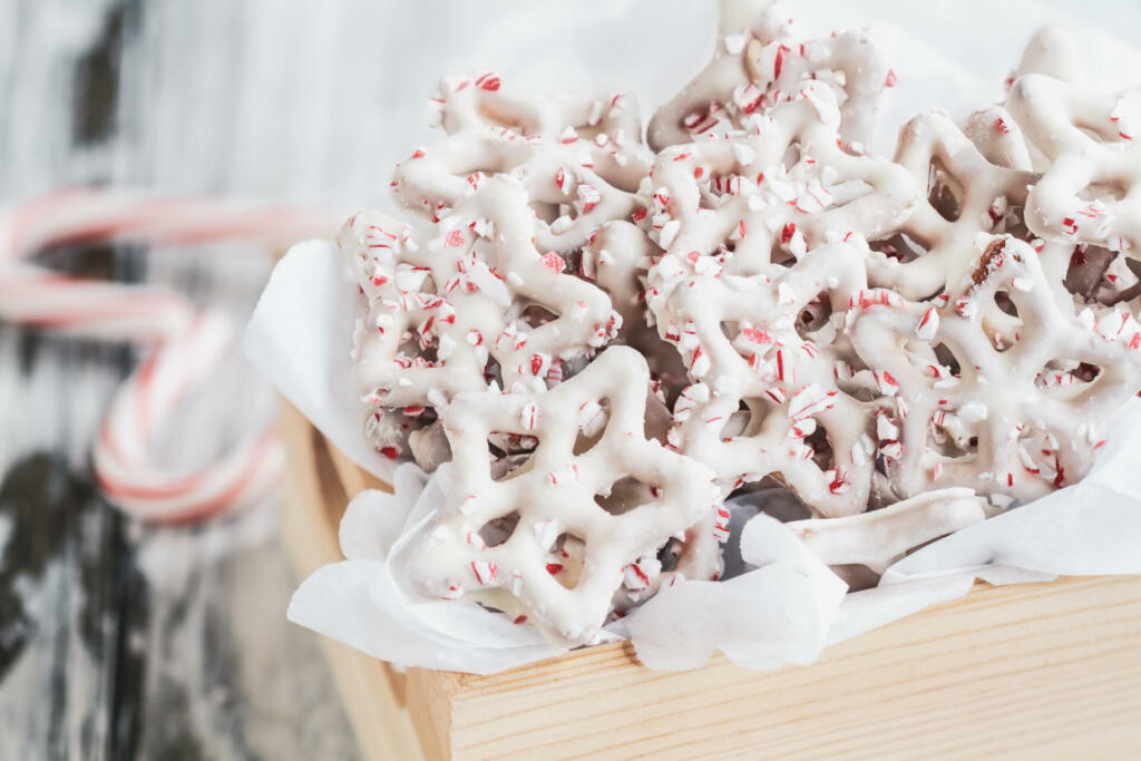 Homemade white chocolate or yogurt covered pretzels with pieces of crushed candy cane. Selective focus with blurred foreground and background. Heart shaped canes on the table.