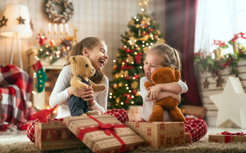 Merry Christmas and Happy Holidays! Cheerful cute childrens girls opening gifts. Kids wearing pajamas having fun near tree in the morning. Loving family with presents in room.