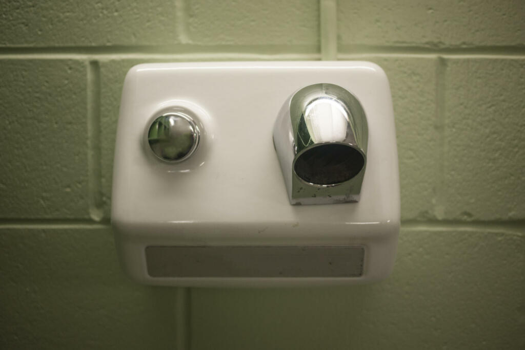 Old white and chrome electric hand dryer on a concrete wall in a school changing room.