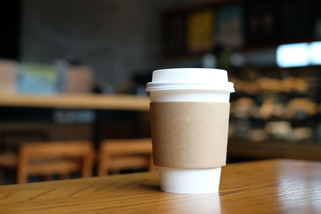 Paper cup with hot drink on wood table in coffee cafe.