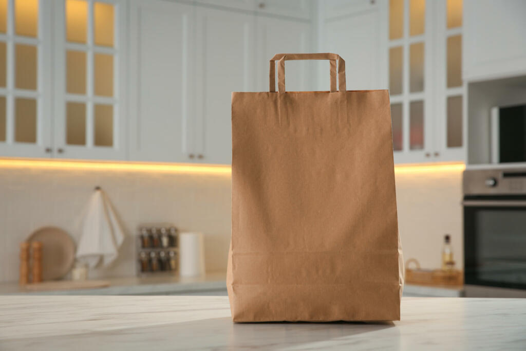 Paper shopping bag on white marble table in kitchen. Space for text