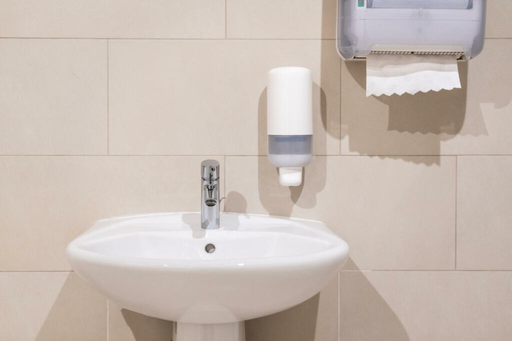 Sink next to soap dispenser pump and a paper towel dispenser