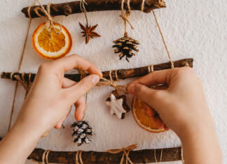 Naravna in preprosta božična dekoracija za tople in domačne praznike Woman hands decorating handmade craft Christmas tree made from sticks and natural materials hanging on wall. Sustainable Christmas, zero waste, plastic free, eco friendly.