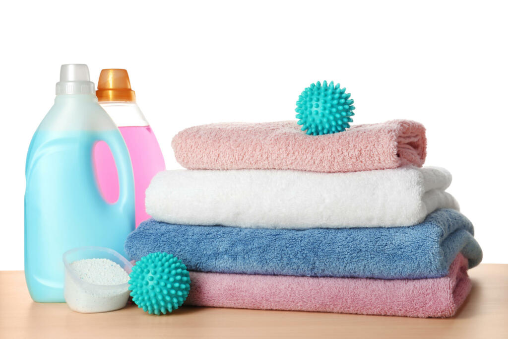 Dryer balls, detergents and stacked clean towels on wooden table against white background