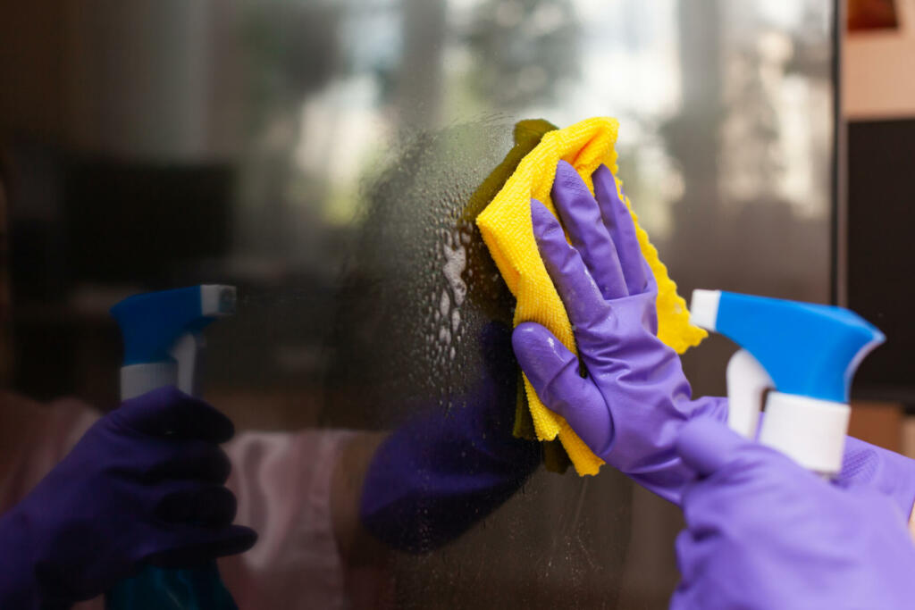 hand in a purple glove wipes the TV screen with a rag, close up