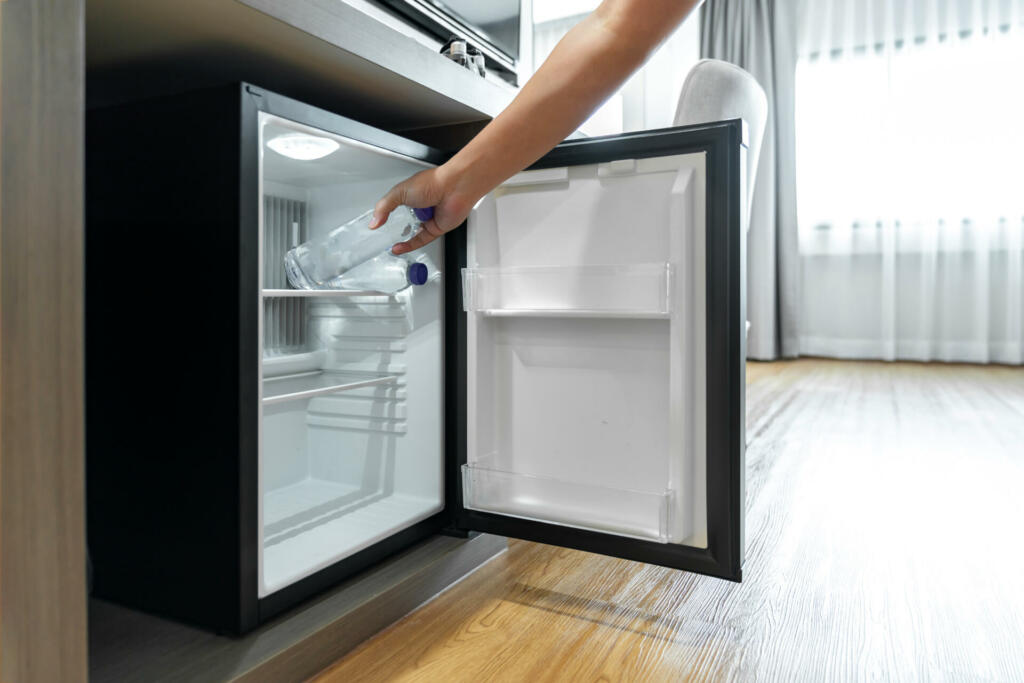 Man Hand opened mini small refrigerator and reached drinking plastic water bottle under the wood counter in the hotel resort bedroom.