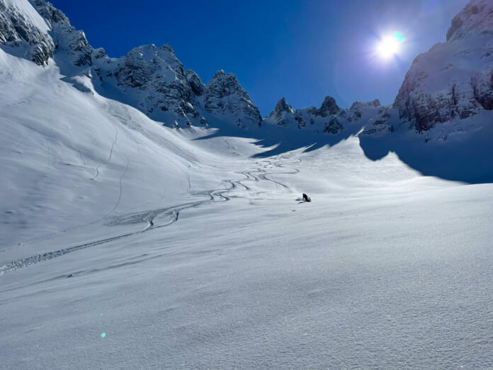 Snowy mountain slope with fresh tracks and skier enjoying on fresh powder. Unrecognizable freeride skier enjoying skiing on fresh snow in the embrace of pristine and snow-covered Albanian mountains.