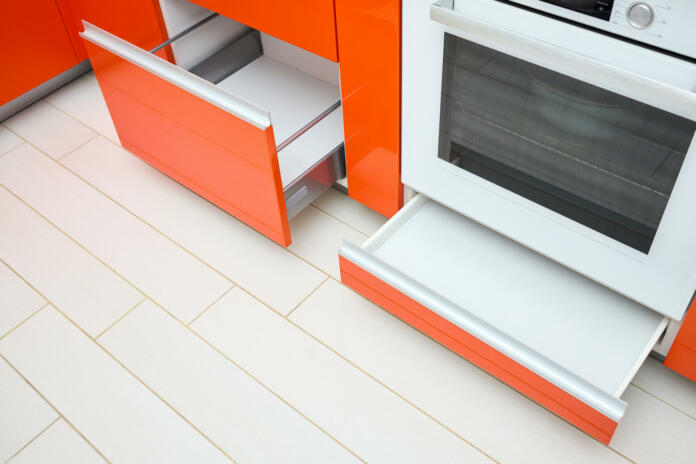 Upscale Maple Red kitchen two drawer for plates or dishes shelf cabinets. Pull out rack cabinets fillers pantry under and near oven. Horizontal drawers shelf with orange front wooden panel, side view.