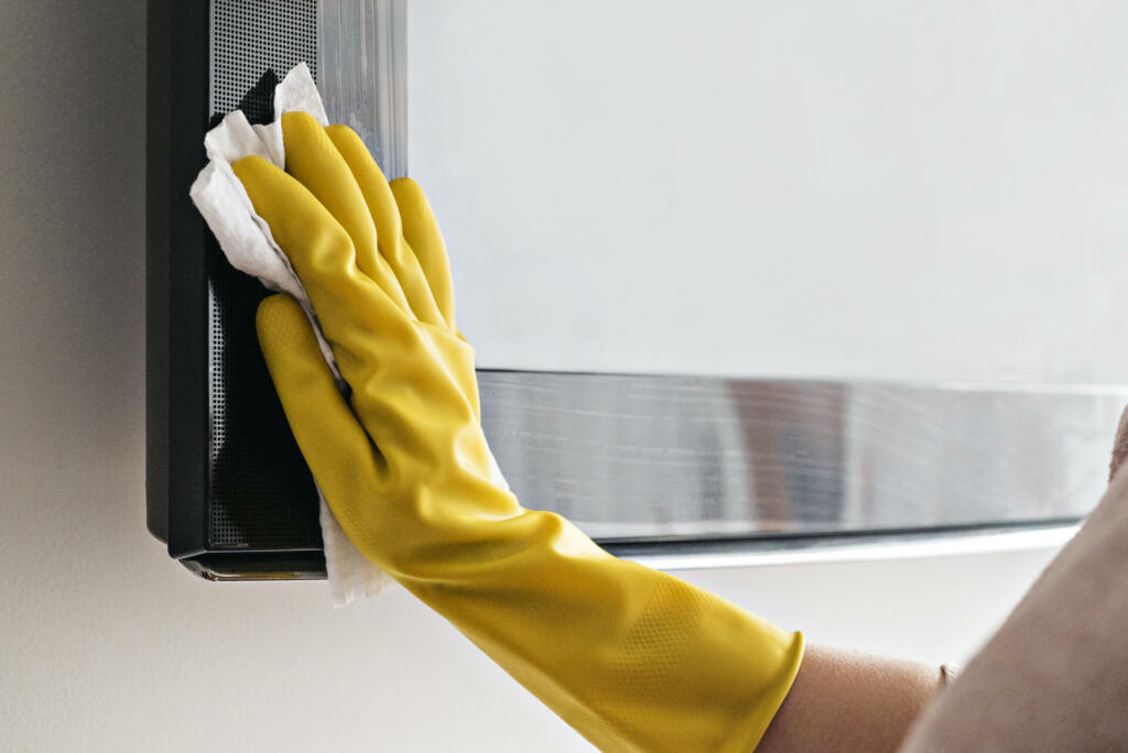 Woman cleaning the TV with damp cloths and wearing yellow gloves during coronavirus, covid 19 quarantine. Maintain hygiene at home, clean dust and bacteria, clean viruses from television.