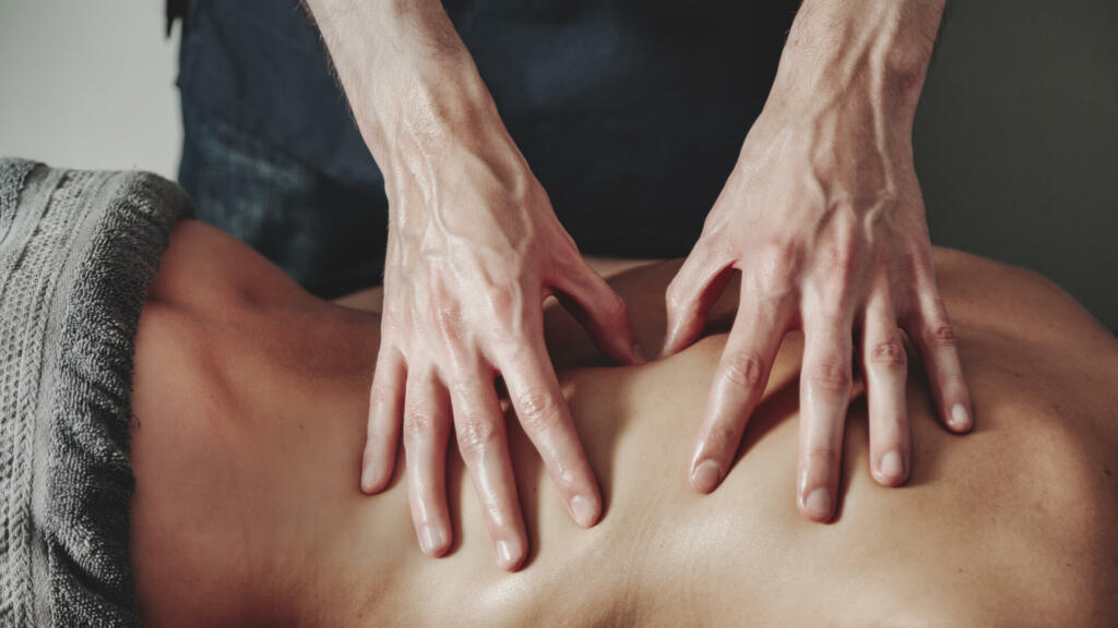 Close up masseur hands doing massage in medical office of fitness room for woman. Professional home massage therapist does massaging exercises. Concept of healthy lifestyle, body care. Copy text space