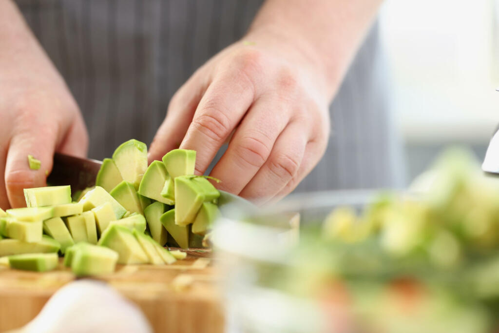 Close-up of man cutting mellow avocado on cutting board, inspiration to cook tasty dinner. Express talent in recipe. Cooking, food, homemade, chef concept