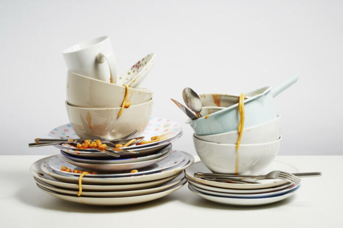 Dirty dishes pile needing washing up. Household chore concept on white background