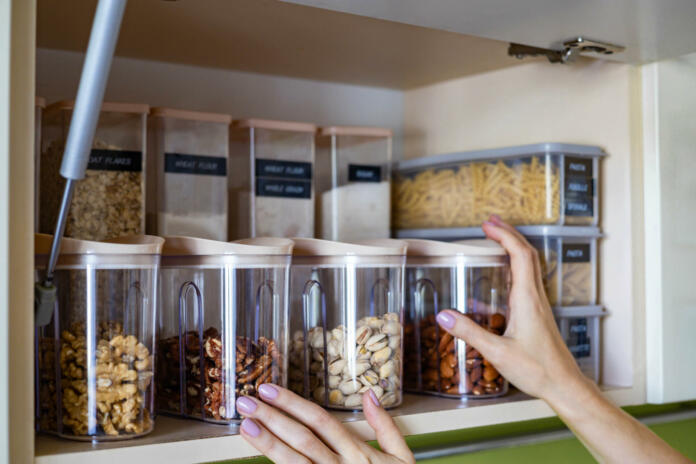 Domestic healthy vegetarian dry food storage organization on shelf at kitchen cupboard. Comfortable neatly keeping arrangement in glass containers oat flakes, wheat flour, sugar, pasta, nuts, rice