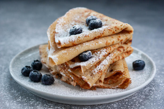 Homemade crepes served with blueberries and powdered sugar on small grey plate