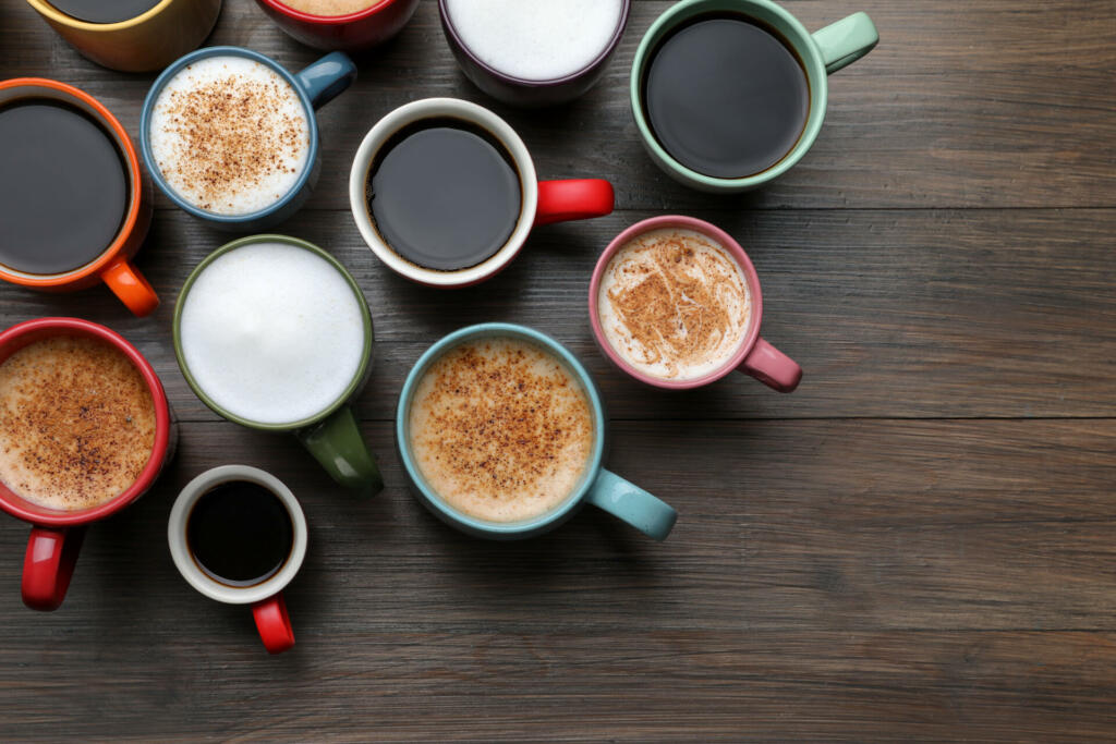 Many different cups with aromatic hot coffee on wooden table, flat lay