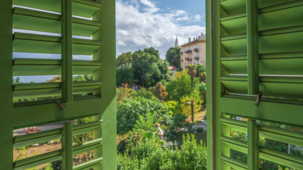 Open window with green wooden shutters with view of the Lovran, travel destination at Istrian seaside in Croatia, selective focus