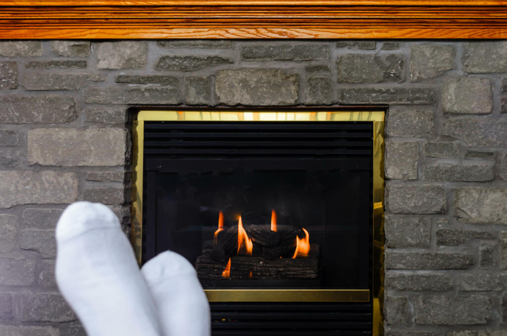 Pair of Pair of blurred adult feet in white socks in front of a small fire in a fireplace with a wooden mantle