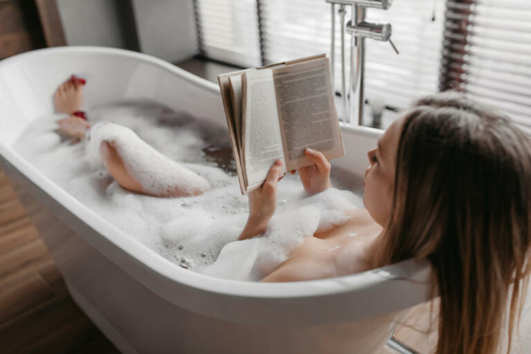 Relaxation and spa day. Carefree woman lying in foamy bath, reading book and enjoying interesting story in relaxing atmosphere in bathtub at home