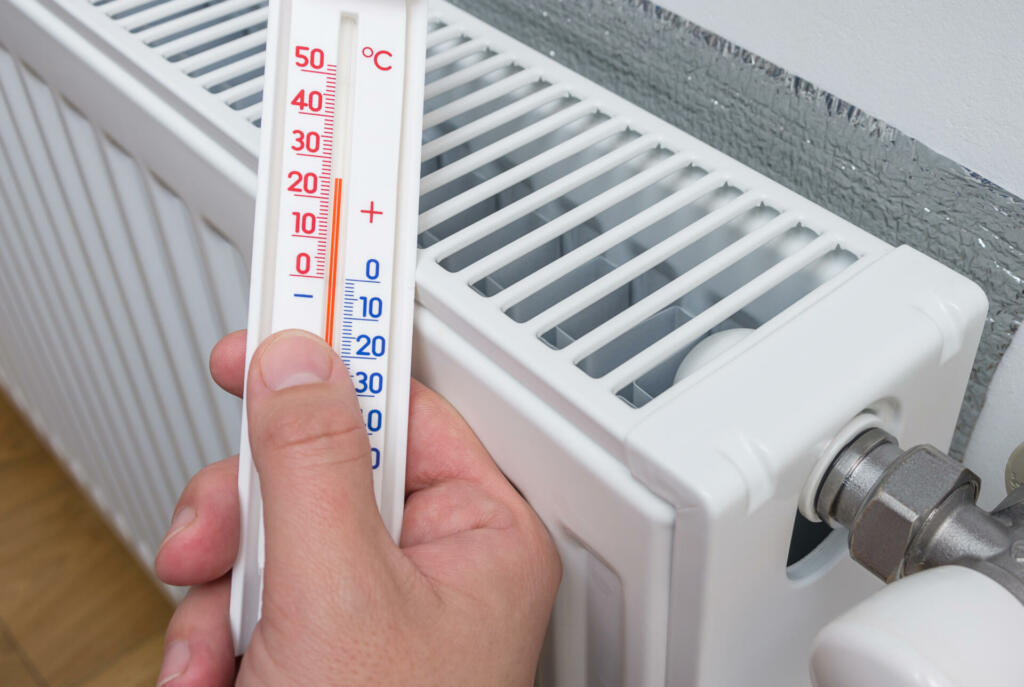 Thermometer in the hand of a person measuring the temperature near a home heater. Celsius temperature scale. Winter heating, concept image.