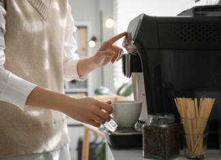 Najboljši kavni aparat: Kako izbrati pravega? Young woman preparing fresh aromatic coffee with modern machine in office, closeup