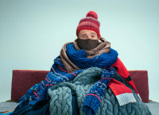 Če imate doma premrzlo, se lahko zgodijo te reči Bearded sick man with flue sitting on sofa at home or studio covered with knitted warm clothes. Illness, influenza, pain concept. Relaxation at Home. Healthcare Concepts.