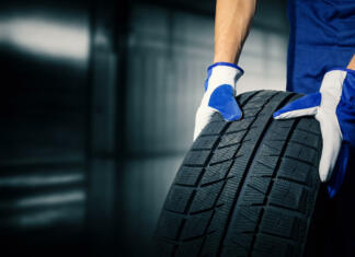 Pozor, zimske pnevmatike niso več obvezne, a nikar ne hitite z menjavo car tire shop and service - mechanic holding new tyre on garage background. copy space