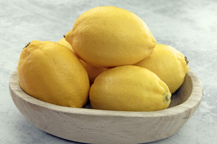 Close up of bright yellow lemons in a natural wooden bowl