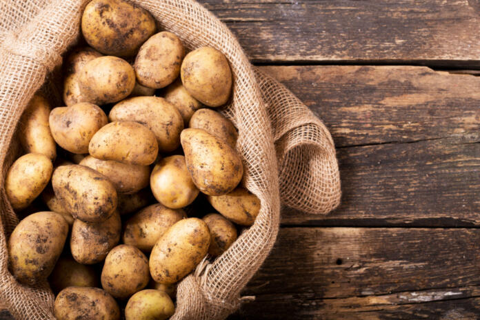 fresh potatoes in sack on wooden table, top view