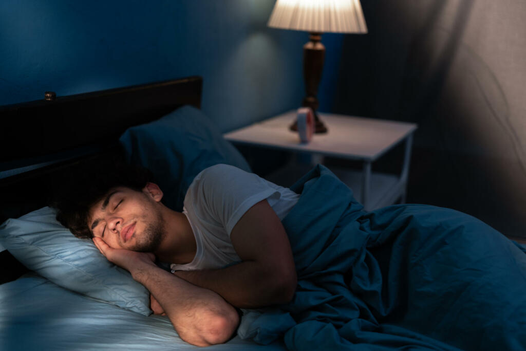 Peaceful young man sleeping in a comfortable bed alone at home, enjoying his orthopedic mattress and cozy pillow. Good sleep concept. Copy space