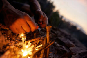Close up of male hands making a fire with flint and steel in the wild. Outdoor adventure, tourism concept