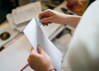 Dobre novice za 364 tisoč ljudi, vsakemu povprečno 262 evrov Close up on girl female woman hands holding and opening white envelope by the table at office work or at home with bills mail or insurance contract invoice letter